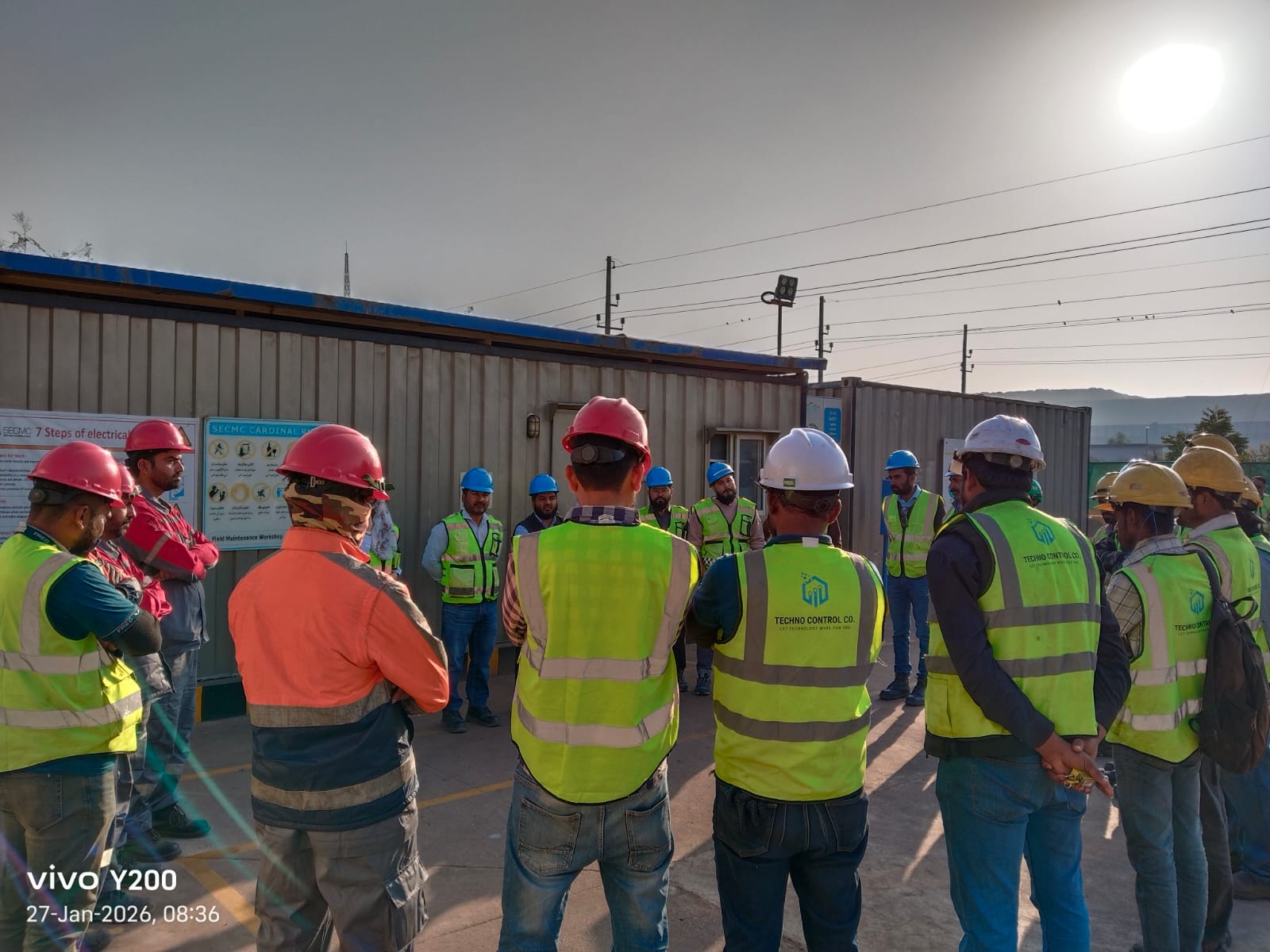 Group of Techno Control Corporation engineers wearing multi-colored safety helmets and high-visibility vests during an on-site briefing.